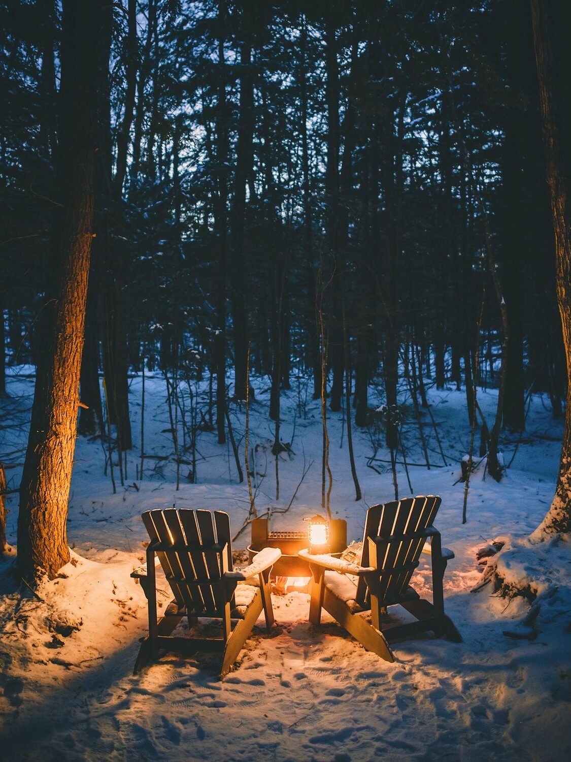 Deux fauteuils adirondacks devant un feu d'extérieur au milieu de la neige